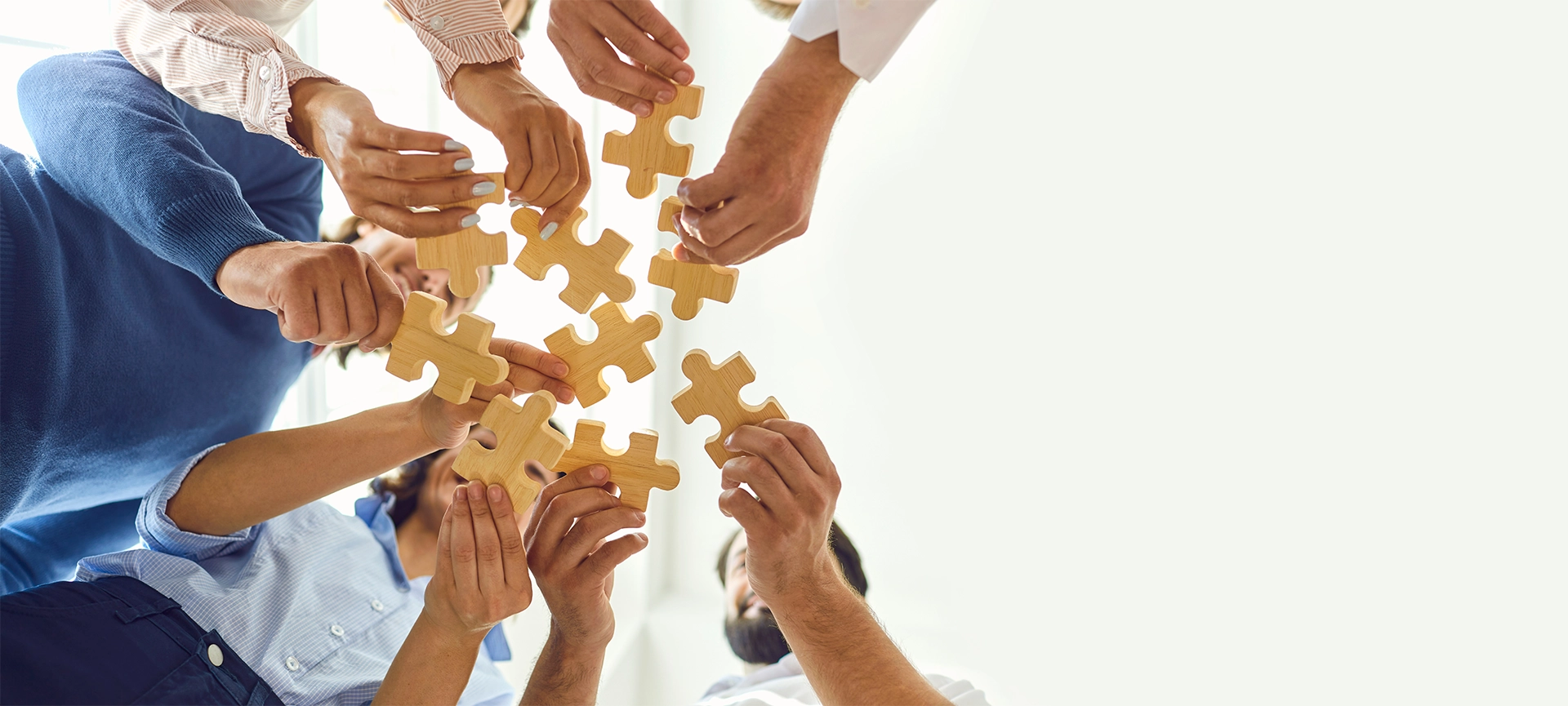 Concept of finding solution. From below of company workers assembling pieces of jigsaw puzzle in work meeting. Banner with happy office employees playing game during team building activity