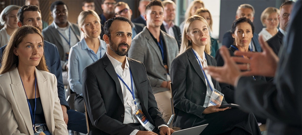 Backview Of Environment Specialist Gesturing And Presenting To Audience of Diverse Business Leaders. Male And Female Attendees Listening To Inspirational Speech On International Economic Forum.